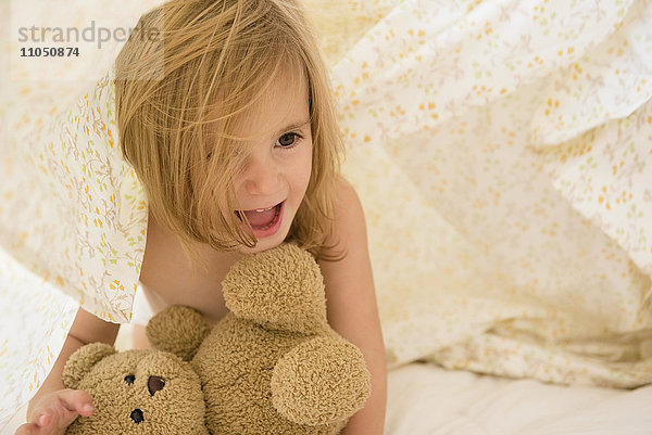 Kaukasisches Mädchen spielt mit Teddybär unter Decken