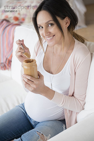 Schwangere kaukasische Frau isst Erdnussbutter aus einem Glas