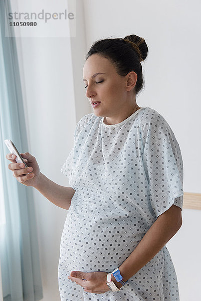 Schwangere kaukasische Frau benutzt Mobiltelefon im Krankenhaus