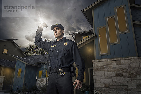 Weißer Polizist leuchtet mit einer Taschenlampe in der Nähe eines Hauses