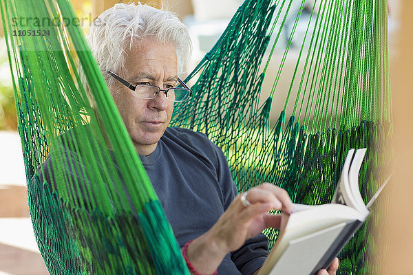 Kaukasischer Mann liest Buch in grüner Hängematte