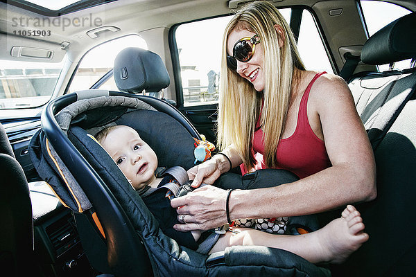 Mutter schnallt ihren kleinen Sohn in den Autositz