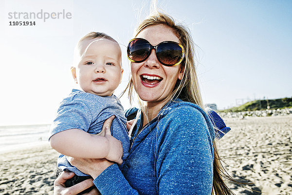 Lächelnde Mutter hält ihren kleinen Sohn am Strand