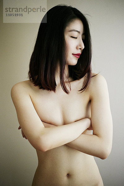 Nackte asiatische Frau mit verschränkten Armen  die die Brüste bedecken