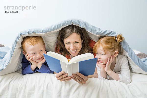 Kaukasische Mutter und Kinder lesen ein Buch im Bett