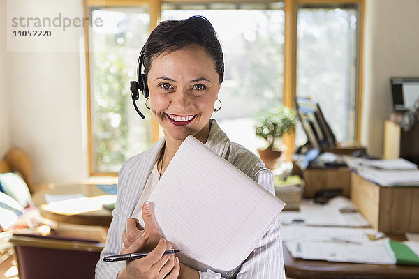 Geschäftsfrau mit Notizblock und Headset im Büro