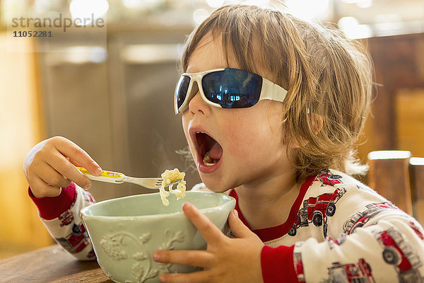 Kaukasischer Junge mit Sonnenbrille beim Essen in der Küche