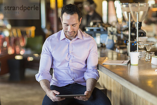 Hispanischer Geschäftsmann benutzt digitales Tablet in einem Café