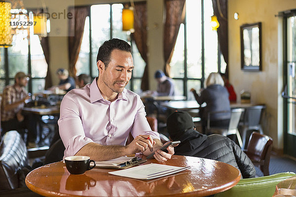 Hispanischer Geschäftsmann benutzt Mobiltelefon in einem Café