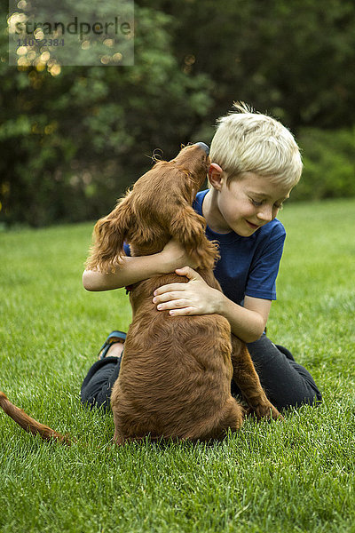 Kaukasischer Junge umarmt Hund im Gras