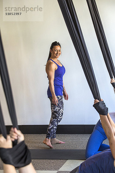 Yogalehrer beobachtet Yogaschüler  die an Seilen hängen