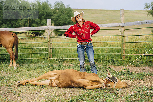 Kaukasisches Cowgirl lächelt mit angebundenen Rindern auf einer Ranch