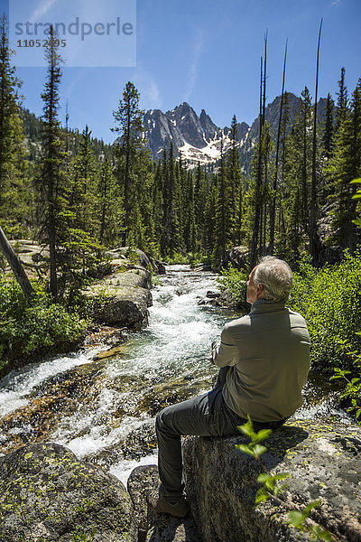 Kaukasischer Mann sitzt auf einem Felsen am Bergfluss