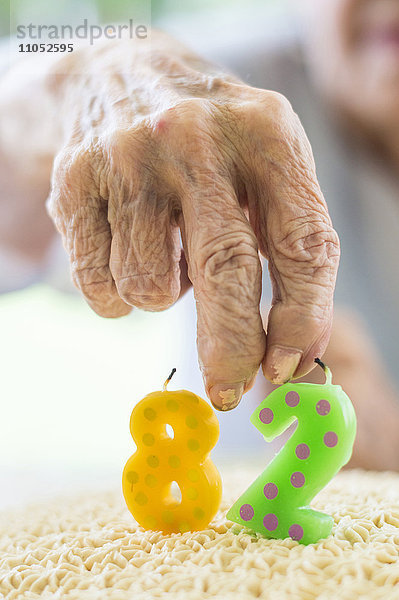 Nahaufnahme einer faltigen Hand  die eine Geburtstagskerze hält