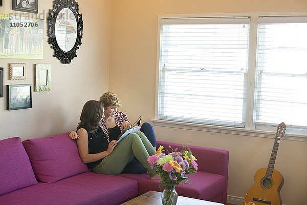 Kaukasisches lesbisches Paar liest Buch auf Sofa