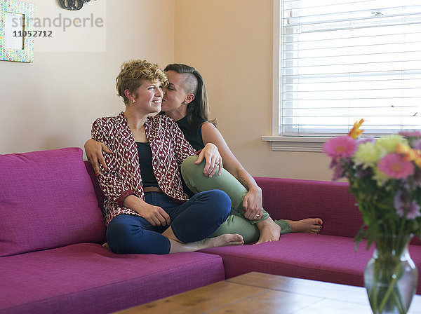 Kaukasisches lesbisches Paar  das sich auf dem Sofa küsst