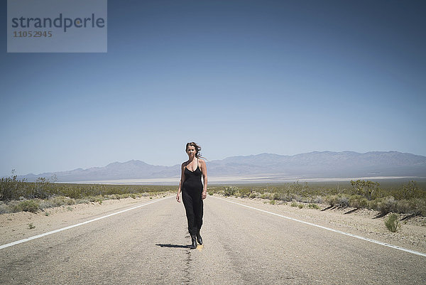 Kaukasische Frau geht auf abgelegener Wüstenstraße