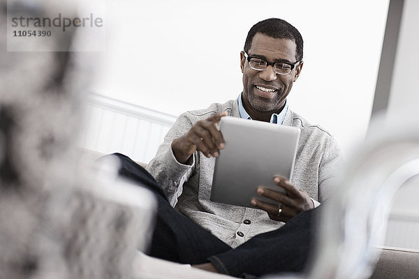 Ein Mann sitzt auf einem Sofa und benutzt ein digitales Tablett.