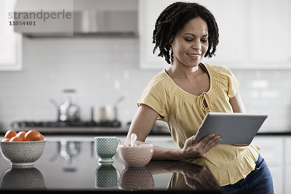 Eine Frau  die zu Hause ein digitales Tablett benutzt. Steht in der Küche.