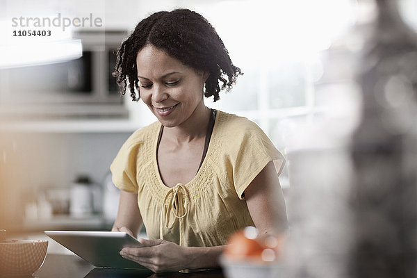 Eine Frau  die zu Hause ein digitales Tablett benutzt. Steht in der Küche.
