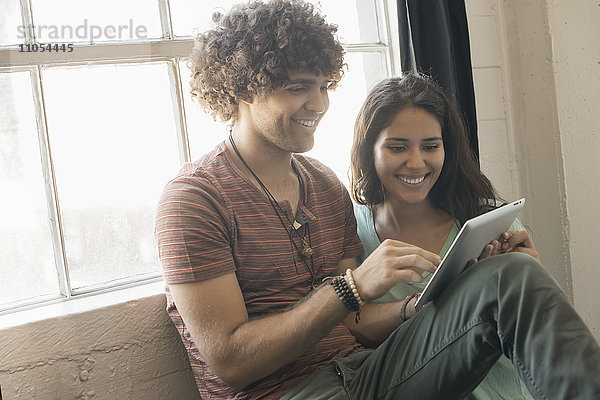 Loft-Wohnen. Ein Mann und eine Frau sitzen am Fenster und benutzen ein digitales Tablett.