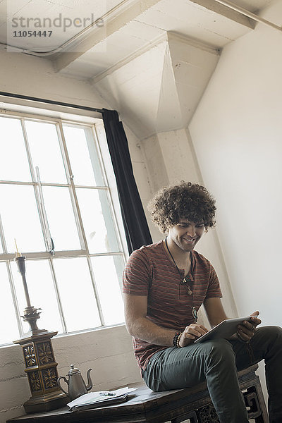 Loft-Wohnen. Ein Mann sitzt am Fenster und benutzt ein digitales Tablett.