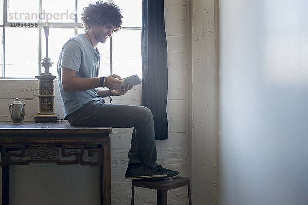 Loft-Wohnen. Ein junger Mann sitzt auf einem Tisch mit einem digitalen Tablett.