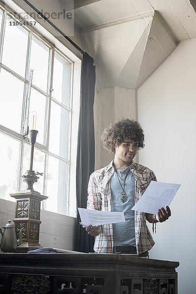 Loft-Wohnen. Ein junger Mann an einem Tisch mit Papierkram in der Hand.