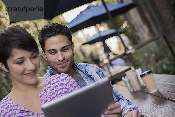 Ein Paar Mann und Frau sitzen in einem Café im Freien und teilen sich ein digitales Tablet.