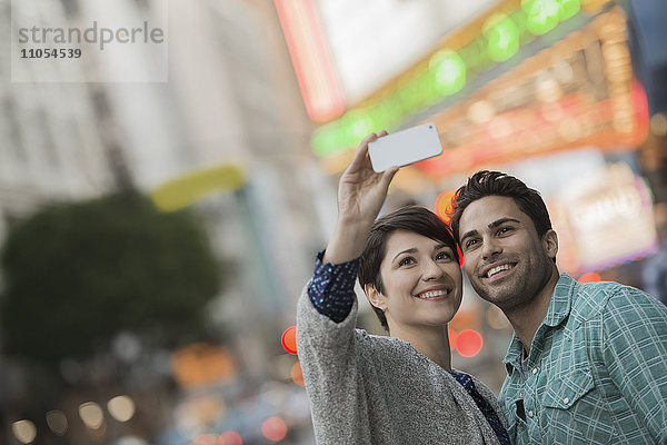 Ein Paar  ein Mann und eine Frau auf einer Straße in der Stadt  die sich mit einem Smartphone ein Selfy nehmen.