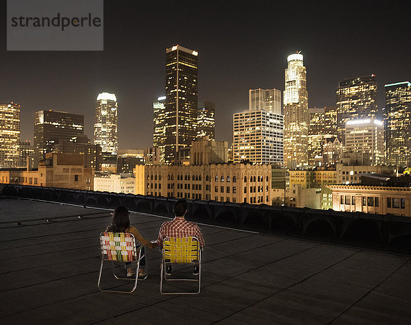 Ein Paar auf einem Dach mit Blick auf Los Angeles bei Nacht  nebeneinander sitzend  mit Blick auf die Stadt.