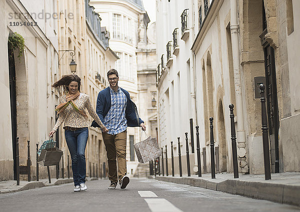 Ein Paar  das mit Einkaufstaschen durch eine schmale Straße in einem historischen Stadtzentrum geht.