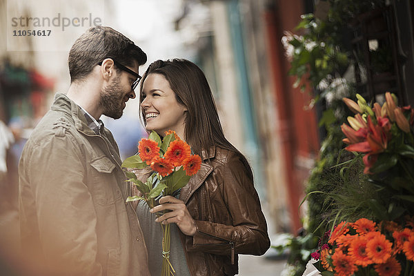 Ein Mann und eine Frau an einem Blumenstand in der Stadt  in der Hand einen Strauß knallroter Blumen.