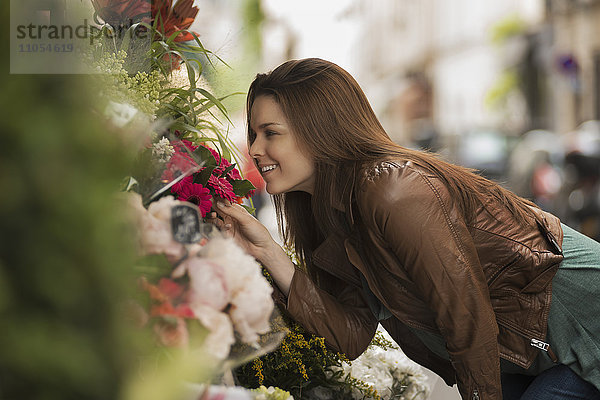 Eine Frau bückt sich  um den Duft von Blumen an einem Stand auf der Straße zu riechen.