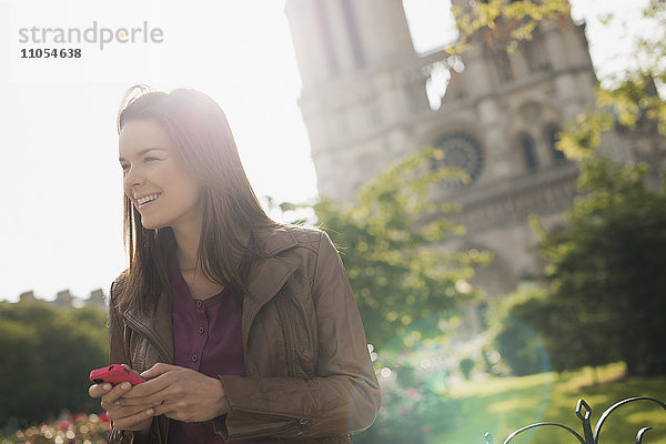 Eine Frau schaut mit einem Smartphone in der Hand in die Ferne vor der Kathedrale Notre Dame in Paris.