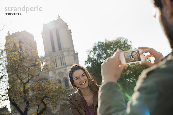 Ein Mann hält ein Smartphone in der Hand und fotografiert eine Frau vor der Kathedrale Notre Dame.