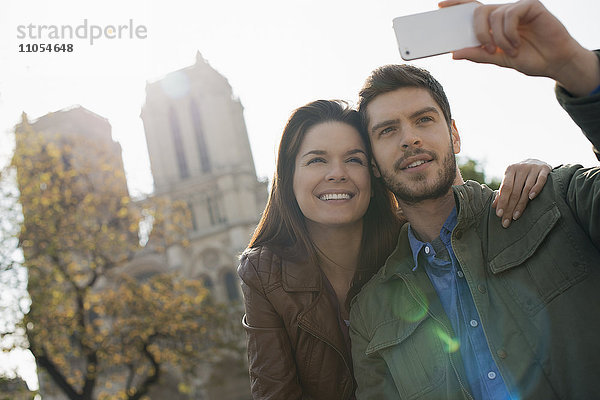 Ein Mann hält ein Smartphone in der Hand und nimmt sich und seine Freundin vor der Kathedrale Notre Dame in Augenschein.