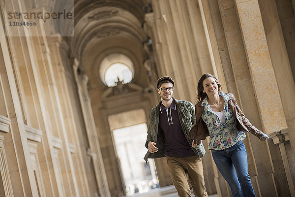 Ein junges Paar geht eine Kolonnade im historischen Herzen einer Stadt hinunter.