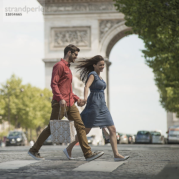 Ein Paar  das Hand in Hand Einkaufstaschen trägt und die Straße an einem historischen Denkmal im Herzen einer europäischen Stadt überquert.