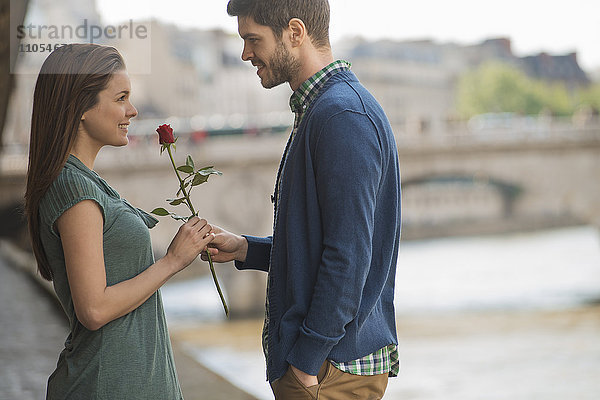 Ein Paar in einer romantischen Umgebung an einem Fluss. Ein Mann bietet einer Frau eine rote Rose an.