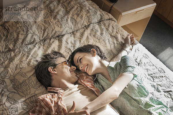 Ein junges Paar liegt Seite an Seite auf dem Bett in einem Motelzimmer.