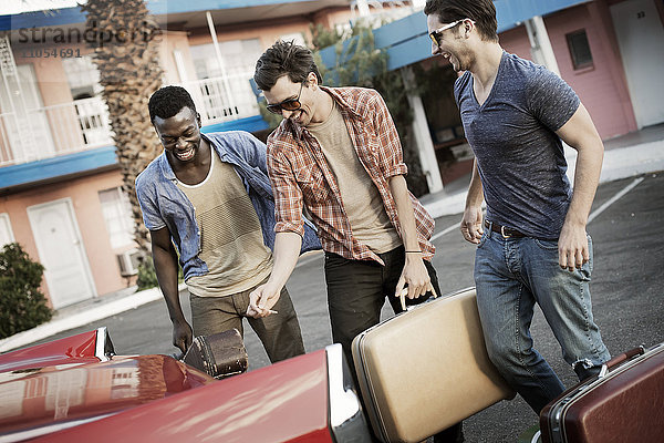 Drei junge Männer  Freunde  die das Auto mit Koffern und einer Gitarre für eine Autoreise packen.