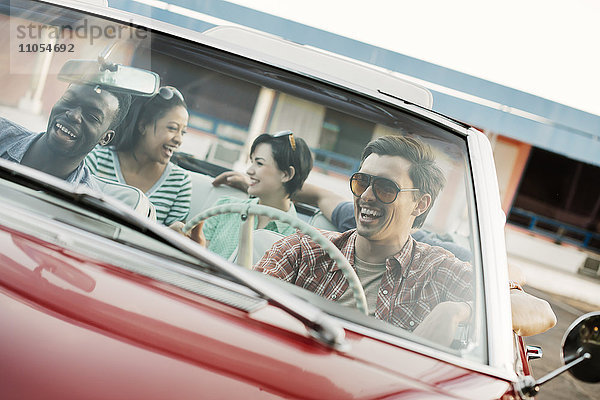 Eine Gruppe von Freunden in einem roten Cabriolet auf einer Autoreise.
