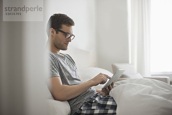 Ein Arbeitstag. Ein Mann sitzt im Bett und benutzt ein digitales Tablett mit Touchscreen.
