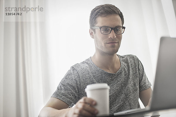 Ein Arbeitstag. Ein Mann sitzt an einem Laptop-Computer und arbeitet in einem Hotelzimmer bei einer Tasse Kaffee.