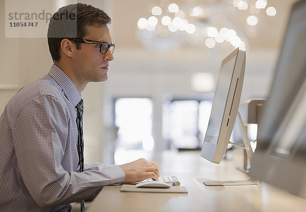 Ein Geschäftsmann in Hemd und Krawatte  der an einem Computer in einem Geschäftszentrum oder Büro sitzt.