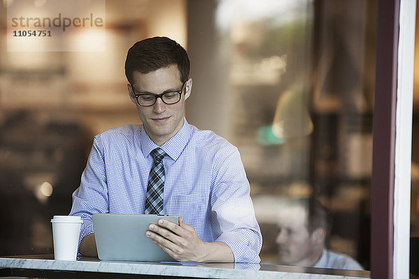 Ein Arbeitstag. Ein Geschäftsmann in Hemd und Krawatte sitzt mit einem digitalen Tablett in einem Café.