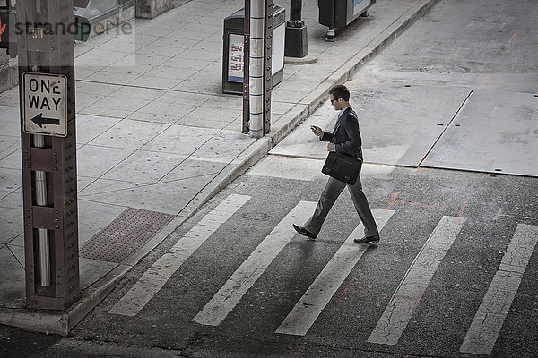 Blick von oben auf einen Mann  der mitten auf einem Fußgängerüberweg steht und auf sein Telefon schaut.