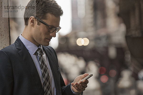Ein Arbeitstag. Ein Geschäftsmann in Arbeitsanzug und Krawatte auf einer Straße in der Stadt  der auf sein Telefon schaut.