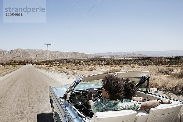 Ein junges Paar  Mann und Frau in einem hellblauen Cabriolet auf offener Straße